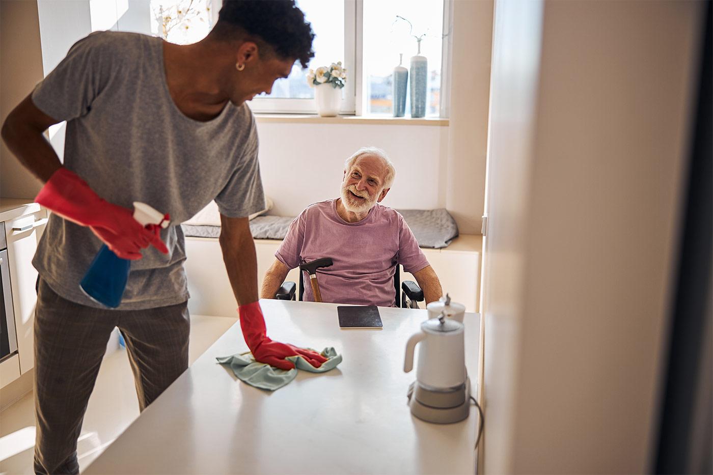 Housekeeping staff cleaning senior apartment at The Commons in Grand Junction while resident relaxes comfortably